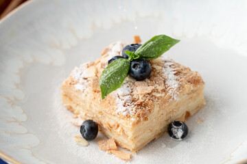 Close up of airy napoleon cake with puff pastry and custard, decorated with blueberry and mint in a fancy restaurant