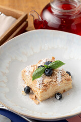Close up of airy napoleon cake with puff pastry and custard, decorated with blueberry and mint in a fancy restaurant