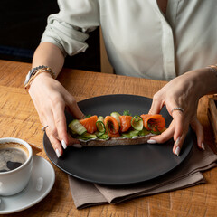 Woman elegantly and neaty eating salmon bruschetta in a restaurant, close up of young beautiful female hands