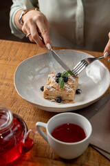 Woman is eating napoleon cake in a restaurant with knife and fork