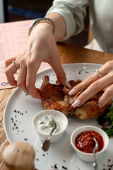 Woman is eating a roasted quail with hands in a restaurant
