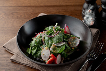 Summer salad with spinach and radish, dressed with crushed pistachio nuts in a black designed bowl in a fancy restaurant