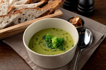 Green broccoli cream soup with olive oil and bread basket aside