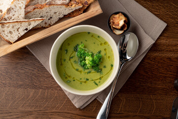 Top view of healthy green broccoli soup on wooden rustic table with linen cloth on it, top view, brad and spoon aside