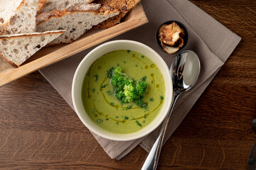 Top view of healthy green broccoli soup on wooden rustic table with linen cloth on it, top view, brad and spoon aside