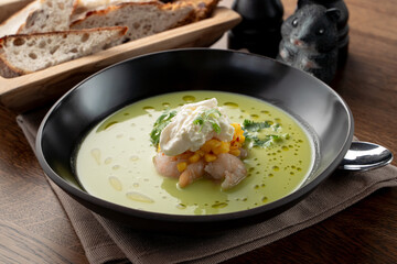 Creamy green soup with crab meat and shrimps on wooden table in a fancy fish restaurant, soft light