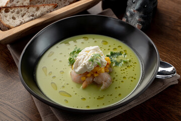 Creamy green soup with crab meat and shrimps on wooden table in a fancy fish restaurant, soft light