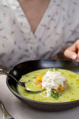 Woman is eating green pea cream soup with seafood with a spoon, close up, hands only visible
