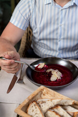Man in a crop sleeves shirt eating cold beetroot soup at a verandah table, close up, hands only visible