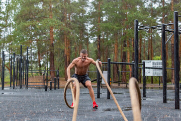 Photo of a man having hard workout with a ropes outdoor in a rainy day.