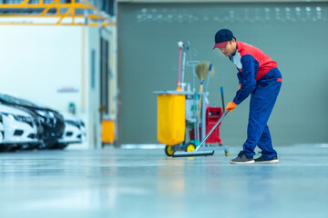 Asian worker in car mechanic repair service center cleaning using mops to roll water from the epoxy...