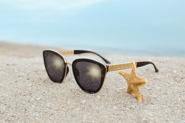 Fototapeta na wymiar Stylish sunglasses and starfish on sandy beach