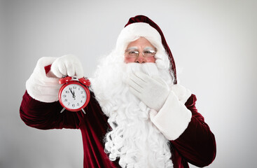 Santa Claus holding alarm clock on light grey background. Christmas countdown