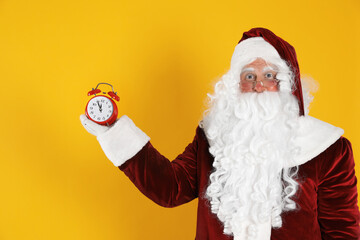 Fototapeta na wymiar Santa Claus holding alarm clock on yellow background. Christmas countdown