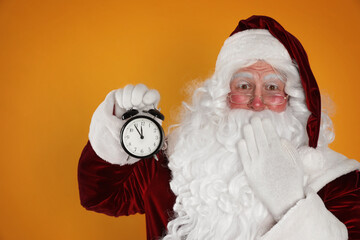 Santa Claus holding alarm clock on yellow background. Christmas countdown