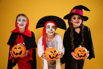 Cute little kids with pumpkin candy buckets wearing Halloween costumes on yellow background © New Africa