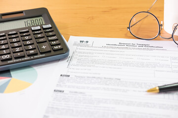Fototapeta premium Selective focus Calculator button. American US tax form on wooden table. With blurred calculator, pen and glasses. Taxation time obligation for people who has income that need to comply to regulation.