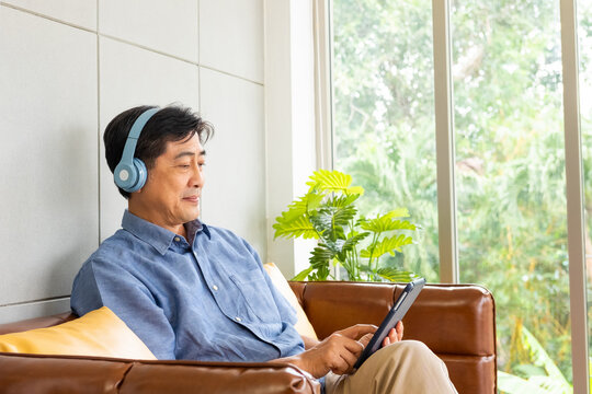 Senior Asian grandfather enjoy and while listening music or watch movie from wireless headphone that streaming music from smartphone or tablet device. Elderly retirement lifestyle. Active senior.