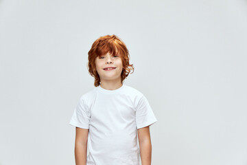 Smiling redhead boy in white t-shirt looking upstairs gray studio background 