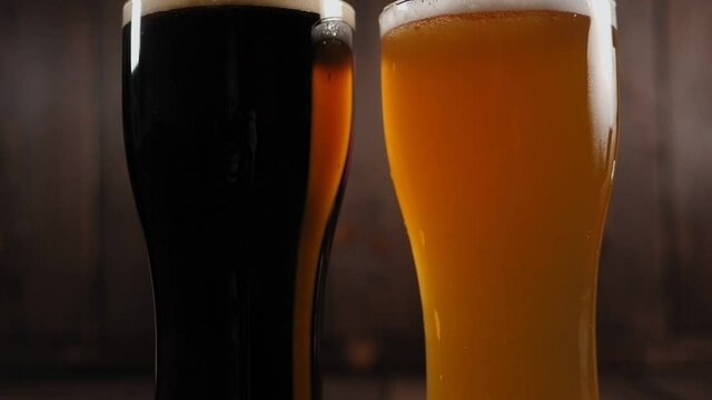 Close-up of two glasses of craft beer on a wooden background, dark beer and light beer. Slow motion.