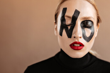 Portrait of blonde girl with red lips on beige background. Woman with word no on face posing with eyes closed