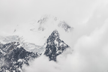 Atmospheric minimalist alpine landscape with massive hanging glacier on snowy mountain peak. Big balcony serac on glacial edge. Low clouds among snowbound mountains. Majestic scenery on high altitude.