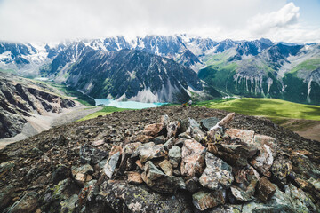 Fototapeta na wymiar Mountaintop tour on peak overlooking scenic valley with big beautiful mountain lake surrounded by giant rocky ranges and glaciers. Man-made stony pile and people on top. Majestic wilderness nature.