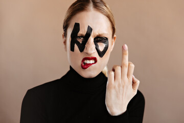 Woman with ponytail dressed in black sweater shows middle finger. Closeup portrait of angry girl...