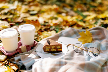 Obraz na płótnie Canvas picnic in the autumn park. A piece of chocolate cake with coffee to go on a blanket next to glasses and a smartphone against a background of maple leaves.