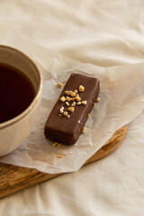 Cup with tea and a chocolate bar on a wooden board next to an open book on a white bed