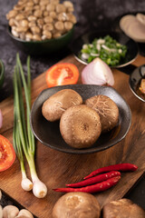 Shiitake mushrooms with garlic, tomato, capsicum, spring onion and red onions on a black cement floor.