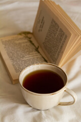 A cup of tea next to an open book on a white bed