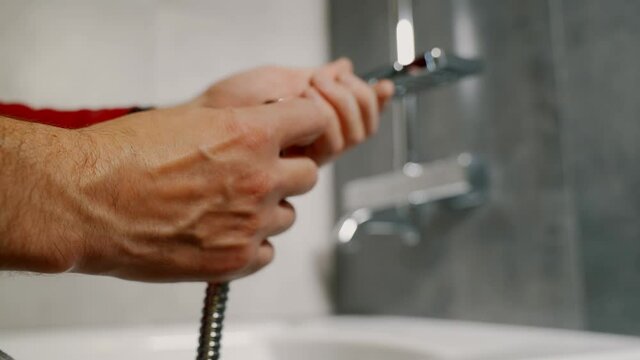 Close-up male hands screw the hose to the shower head.