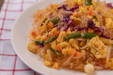 Stir fried glass noodles with eggs and put on a plate on a red white cloth.