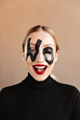 Joyful girl with red lips winks. Portrait of woman with word no on her face dressed in black sweater