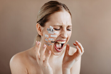 Blond sad woman with stickers on face shouts on beige background
