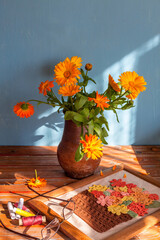 Calendula bouquet in an old clay pot and handicrafts in the foreground, Tver region, Russia