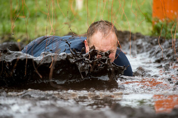 Mud race runners. Crawling,passing under a barbed wire obstacles during extreme obstacle race....