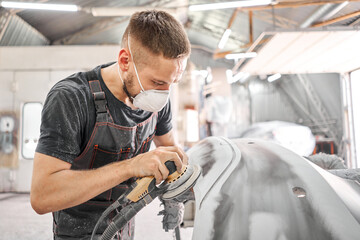 The mechanic works with a grinding tool. Sanding of car elements. Garage painting car service. Repairing car section after the accident. - 384314357