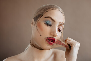 Portrait of woman tearing on herself mask with applied makeup