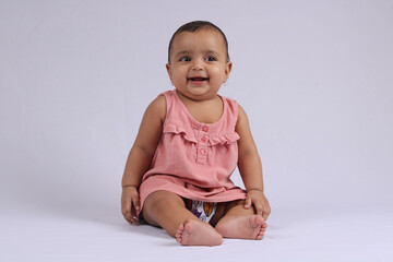 cute Indian cheerful baby sitting and smiling over white.