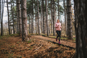 Young smiling sportswoman with healthy habits running in woods at autumn and preparing for marathon.