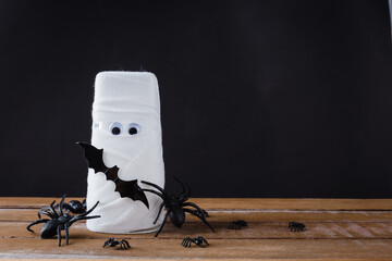 Funny Halloween day decor party concept, The mummy ghost on water glass wrapped around with bandage and have bats and spider stick it found only eyes, studio shot isolated on black background