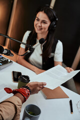 Close up of male hand holding, giving a script paper to female radio host during a live show in studio