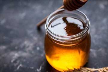 Jar with freshly harvested liquid honey on the old wooden table. Selective focus.