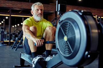Sport and fitness after 50. Strong mature athletic man in sportswear exercising on rowing machine...