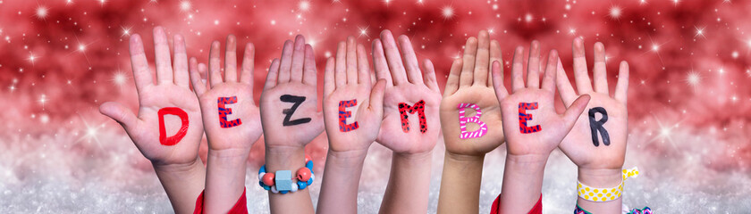 Children Hands Building Colorful German Word Dezember Means December. Red Snowy Christmas Winter Background With Snowflakes And Sparkling Lights