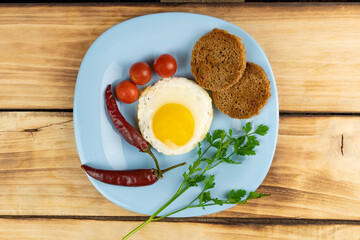 Top view of a fried egg, two chilli toast and cherry tomatoes on a blue plate. Wooden background.