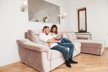 Fototapeta premium young couple bearded man and woman with mobile gadget sitting on sofa at comfort home online