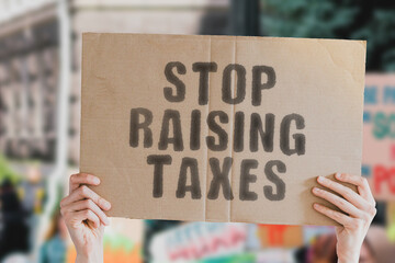 The phrase " Stop raising taxes " on a banner in men's hand with blurred background. Taxation. Tax. Business. Money. Revenue. Government. Charges. Raise. Protest. Liberation